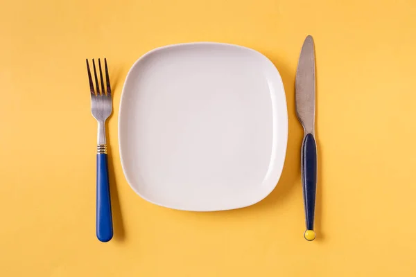 Food background with empty white plate and cutlery , over yellow background, flat lay.