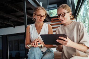 İki kadın, modern bir ofis ortamında etkili bir işbirliği sergileyen bir tabletle düşünceli bir şekilde nişanlanıyor.
