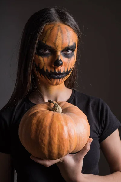 Porträt eines schrecklich geschminkten Mädchens zu Ehren von Halloween auf schwarzem Hintergrund mit einem Kürbis — Stockfoto