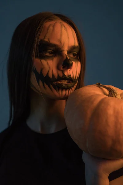 Een meisje in een dode mans masker met een pompoen op een donkere achtergrond. Halloween — Stockfoto