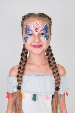 Charming girl with a blue butterfly painted on her face, on white background. face painting