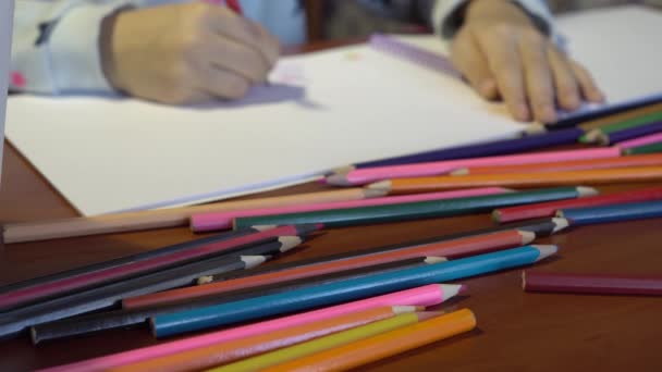 Buntstifte auf dem Tisch verstreut. aus dem Fokus der Kinderhand, die das Album einzeichnet — Stockvideo