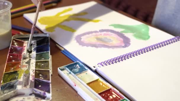 El niño dibuja una flor y el sol en el álbum con pinturas acrílicas — Vídeo de stock