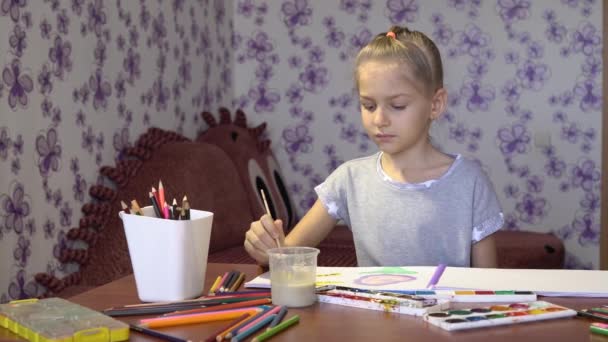 Una niña linda dibuja pinturas de colores en una hoja de papel en su habitación — Vídeo de stock
