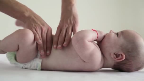 Ребенок в подгузниках лежит на спине и получает массаж живота — стоковое видео