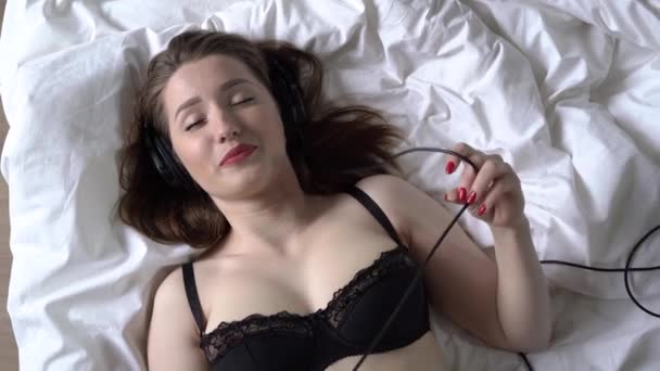 O tânără care ascultă muzică cu căști întinse pe pat — Videoclip de stoc