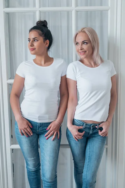 Kaksi kaunista blondi ja brunette tytöt poseeraa valkoinen t-paidat ja farkut — kuvapankkivalokuva
