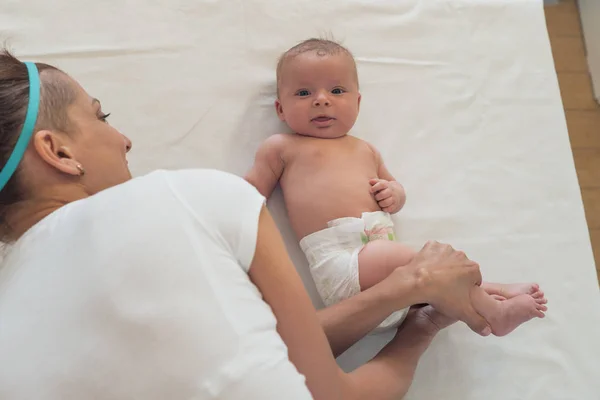 Un retrato de un niño hermoso y una mujer sosteniéndolo en un cambiador. Masaje bebé . —  Fotos de Stock