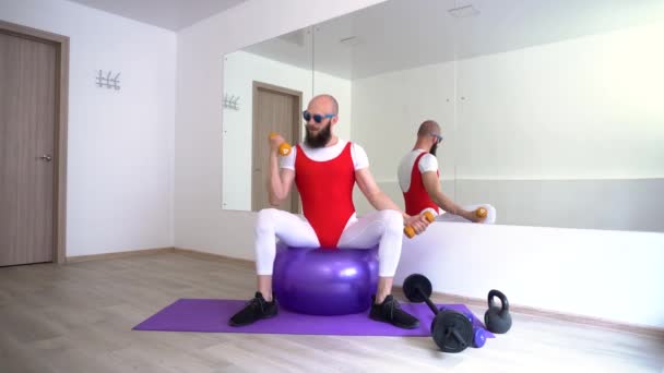 4k halterofilista em leggings fitness apertado aperta as mãos sentado em uma bola grande de borracha — Vídeo de Stock