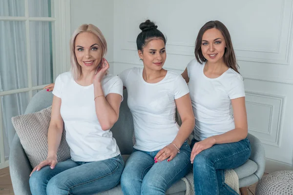 Jonge mooie meisjes in witte T-shirts en jeans zitten op de Bank — Stockfoto