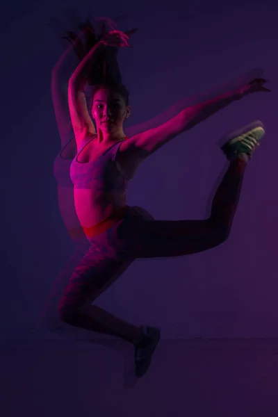 Asian girl gymnast in colored light posing in a jump. — Stock Photo, Image