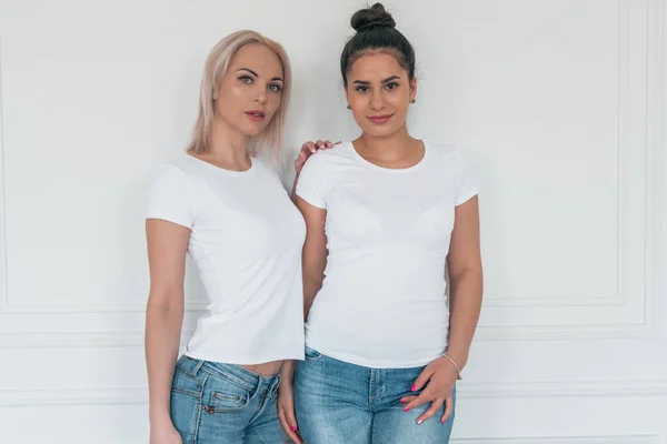 Portret van twee vriendinnen blonde en brunette in witte t-shirts zonder ontwerp — Stockfoto