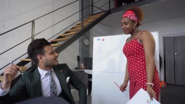 Una ragazza afro-americana mostra un grafico degli investimenti su un flipchart ufficio e risponde alle domande dei colleghi . — Video Stock