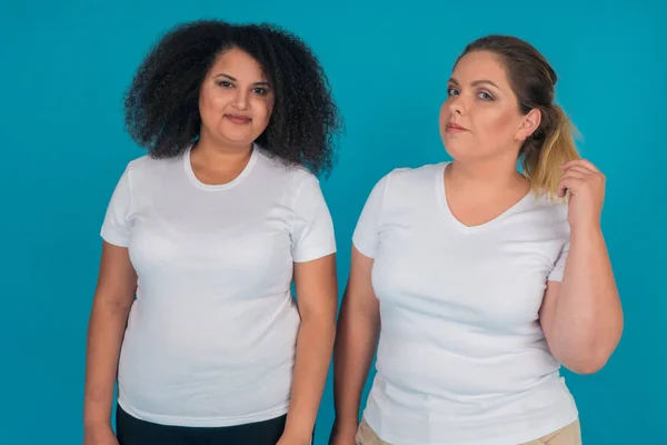 Portrait of multinational girl and Caucasian girl in white t-shirts on blue background. Women with large weight — Stock Photo, Image