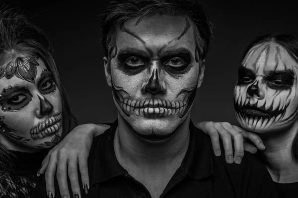 Male and female face art for Halloween. Black and white portrait of a guy and two girls with scary painted faces on a black background. All saints  night.
