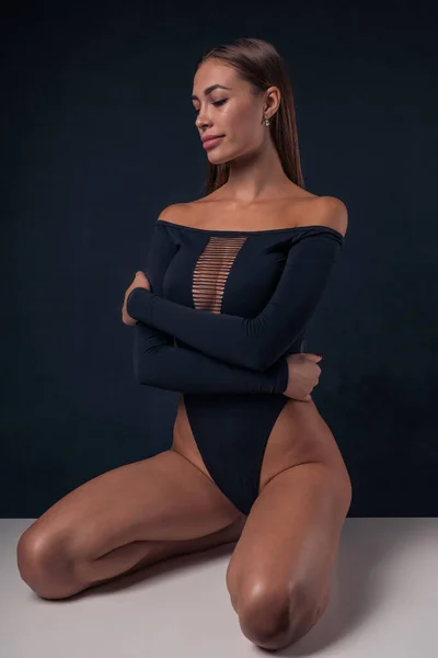 Mulatto flicka klädd i sexig body suit baddräkt poserar sittande på ett bord — Stockfoto
