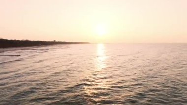 Golden hour shines over the Baltic in Koobrzeg: the lighthouse stands tall, waves shimmer, and the sandy shore fills with silhouettes of evening walkers.