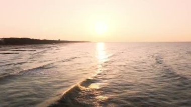 Koobrzeg üzerinde günbatımı antenleri: parlayan gökyüzü ve deniz, uzakta deniz feneri, kumlu sahil altın saatin tadını çıkaran insanlarla dolu.