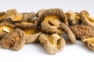 Bu resimde kurutulmuş shiitake mantarları beyaz arka planda ustalıkla sıralanmış, geleneksel mutfak işçiliğini çağrıştıran dokulu yüzeyleri ve derin organik renkleri gözler önüne seriliyor..