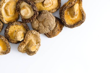 Bu resim, hem geleneği hem de sofistike mutfağı çağrıştıran, detaylı dokuları ve derin toprak tonlarıyla beyaz bir zemin üzerinde zarif bir şekilde düzenlenmiş kurutulmuş shiitake mantarlarını içeriyor..