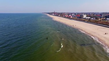 Sarbinowo üzerinde sakin bir bahar günü geniş kumlu bir sahil, huzurlu bir gezinti alanı ve bu küçük Baltık köyünün ikonik kırmızı tuğlalı kilisesini gösterir..