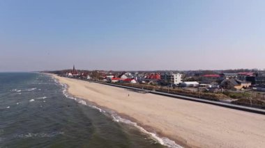 Günışığı Sarbinowo Baltık boyunca uzanır: kumlu plaj, huzurlu gezinti güvertesi ve deniz kenarındaki evlerin yanında tarihi kırmızı tuğlalı kilise..