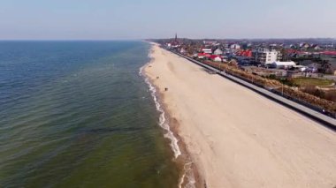 March sunlight illuminates Sarbinowos sandy Baltic coast, the seaside promenade, and the red-brick church among village rooftops.
