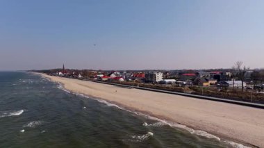 From the drones eye: Sarbinowos sandy beach, calm sea, and promenade stretch along the Baltic with the red-brick church in view.