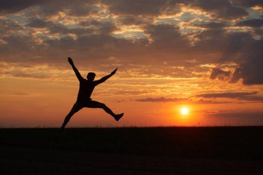 Sevinç, mutluluk ve özgürlük duygusu ile gün batımına karşı atlama bir genç adam silüeti