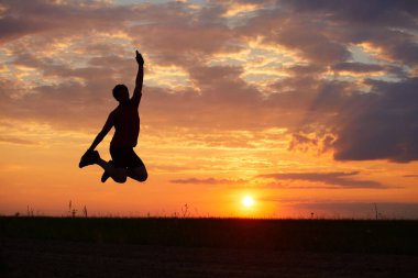 Sevinç, mutluluk ve özgürlük duygusu ile gün batımına karşı atlama bir genç adam silüeti