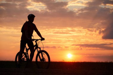Bir gün batımı arka plan alanını giden yolda seyahat eden bir bisikletçi silüeti