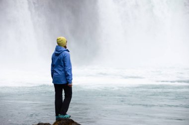 Güzel bir genç kadın güzel bir şelale zemine karşı duruyor. İzlanda