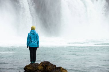 Güzel bir genç kadın güzel bir şelale zemine karşı duruyor. İzlanda