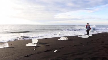 Mutlu bir genç kadın okyanus plaj boyunca çalışır ve llbda taşların üstünden atlar. İzlanda
