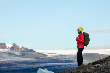Sırt çantası ile sportif kız buz göl ve dağların güzel manzarasına hayran. İzlanda'daki buz lagoon