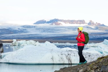Sırt çantası ile sportif kız buz göl ve dağların güzel manzarasına hayran. İzlanda'daki buz lagoon