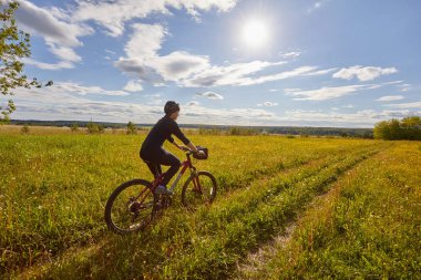 Genç bir kadın bir bisiklet ile bir alan yolda gidiyor. Yaz güneşli gün