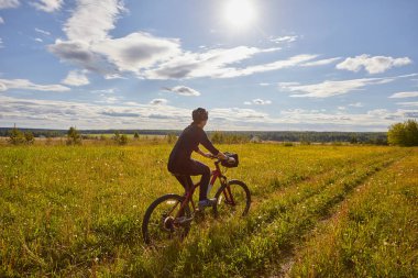 Genç bir kadın bir bisiklet ile bir alan yolda gidiyor. Yaz güneşli gün