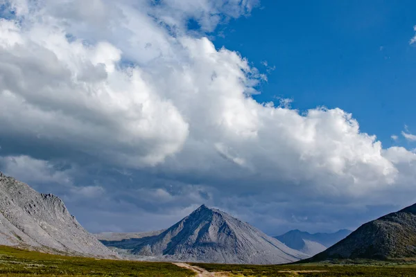 Beautiful mountain landscape. Relax in fresh air. Blue sky with clouds. Mountain peaks with snow and grass. Mountain tundra Ural Russia