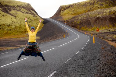 Sarı kız mutlu bir şekilde yürüyor ve asfalt yolda atlar. İzlanda'daki sabah erken gün. İzlanda'da araba Turizm.