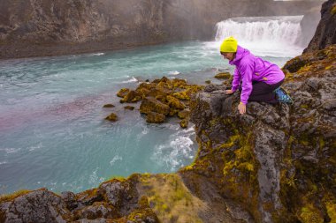 Genç bir kadın hayran olduğu bir şelale üzerinde bir uçurumun kenarında. Seyahat sonbahar manzarası. İzlanda Europe