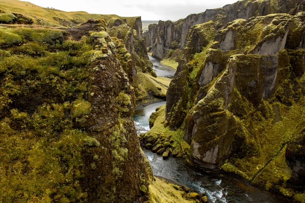 Deep canyon, steep cliffs overgrown with green moss, surrounded by a very fast river with cold water. Canyon of Icelandic tales - Fjardrarglufur