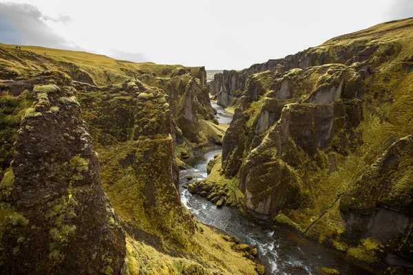 Deep canyon, steep cliffs overgrown with green moss, surrounded by a very fast river with cold water. Canyon of Icelandic tales - Fjardrarglufur