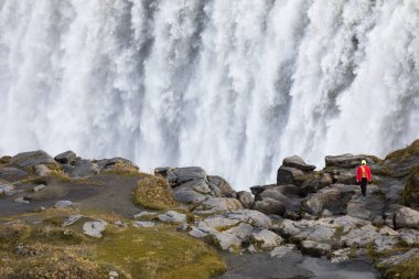 Sarı ön planda ünlü İzlandalı dev Dettifoss Şelalesi ve bir kadın giyinmiş.