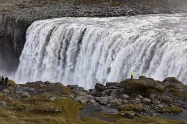 Sarı ön planda ünlü İzlandalı dev Dettifoss Şelalesi ve bir kadın giyinmiş.