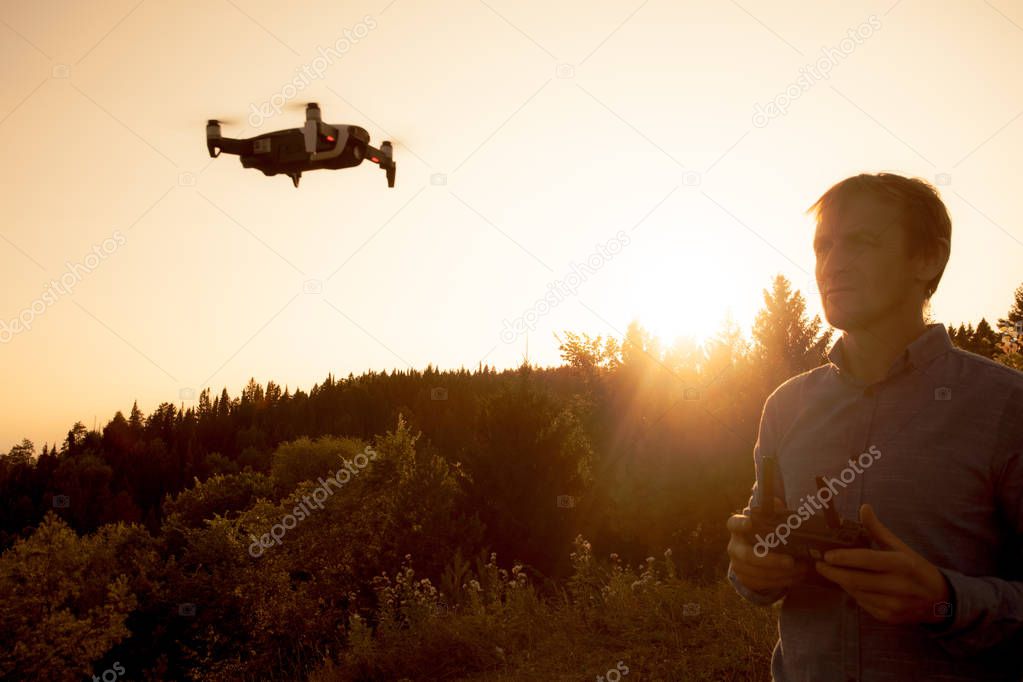 A man launches quadcopter. Flying drone over the river and forest on a sunny day