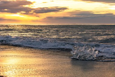 Cliff siyah kumlu bir plaj üzerinde Jokulsarlon beach (Diamond Beach) Güneydoğu İzlanda ile buz. Yükselen güneşin ışığında buz