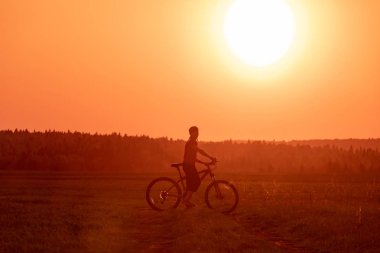 Bir kız parlak bir gün batımı ve sarı güneşin arka planında yolda bir bisiklet sürmek