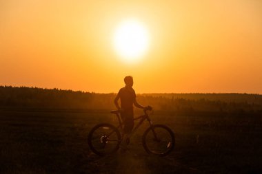 Bir kız parlak bir gün batımı ve sarı güneşin arka planında yolda bir bisiklet sürmek