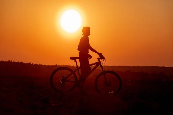 Happy girl with a bicycle on the nature on the background of bright sunset and yellow sun